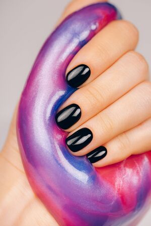 hands with black manicure holding slime in blue and pink vibrant colorsの写真素材