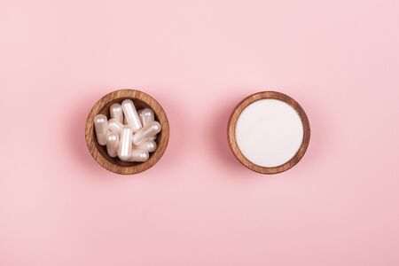 Collagen in capsules and in powder in two wooden bowls on pastel pink backgroundの写真素材
