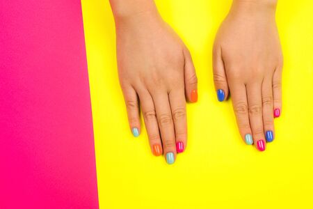 Female hands with perfect manicure in trendy neon colors on bright pink and yellow background. Beauty concept.の写真素材