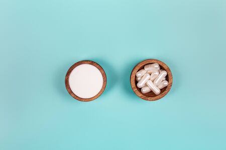 Collagen in capsules and in powder in two wooden bowls on pastel blue backgroundの写真素材