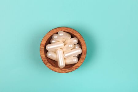 Collagen in capsules in wooden bowl on pastel blue backgroundの写真素材
