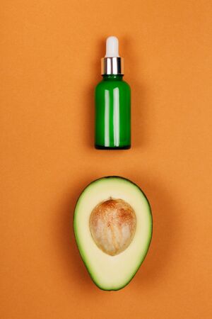 Half avocado with bone and green bottle with beauty oil on orange background. Flat lay style.の写真素材