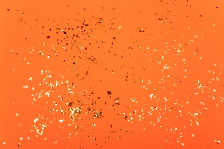 Golden flying sparkles on bright orange background. Festive backdrop for your projects.の写真素材