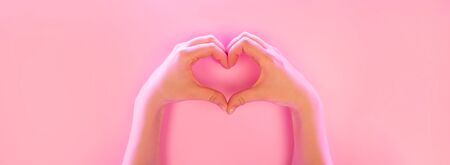 Young woman's hands made gesture of heart shape in trendy neon light on pink background. Love concept.の写真素材