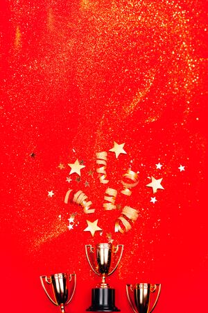 Three golden winner cups with confetti on a red background. Flat lay style. Competitions concept.の写真素材