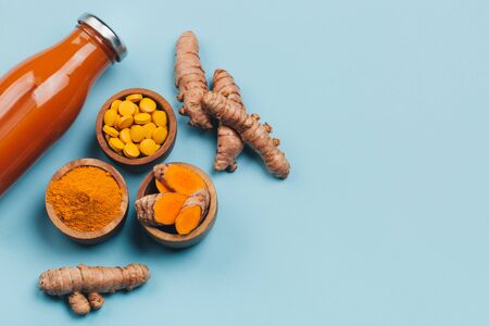 Turmeric in different states: fresh in bottle, pills, powder and cut plant on wooden tray, dry root in wooden bowl.の写真素材