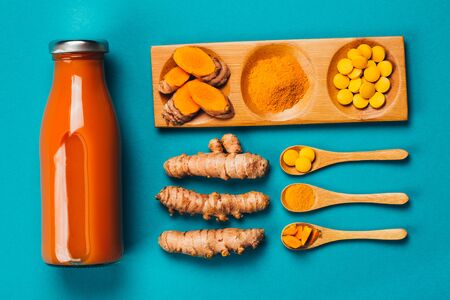 Turmeric in different states: fresh in bottle, pills, powder and cut plant on wooden tray, dry root in wooden bowl.の写真素材
