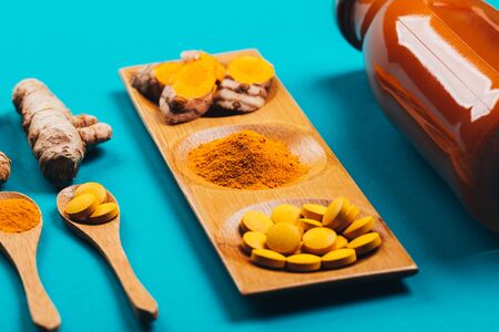 Turmeric in different states: fresh in bottle, pills, powder and cut plant on wooden tray, dry root in wooden bowl.の写真素材
