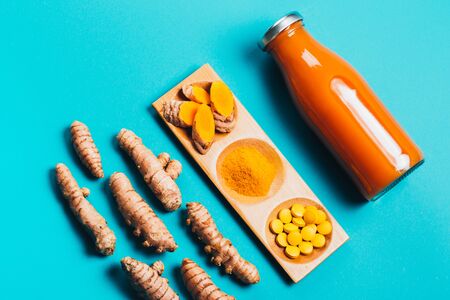 Turmeric in different states: fresh in bottle, pills, powder and cut plant on wooden tray, dry root in wooden bowl.の写真素材