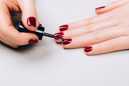 Woman making red manicure by herself on grey background.の写真素材