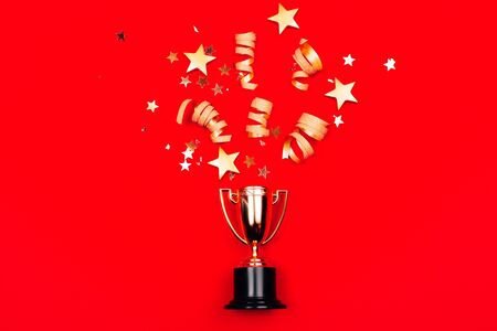 Golden winners cup with confetti on a red background. Flat lay style. Champion concept.の写真素材