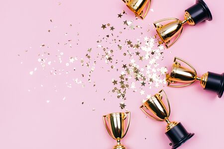 Golden winner cups with sparkles on a pink background with copy space. Festive concept. Flat lay style.の写真素材