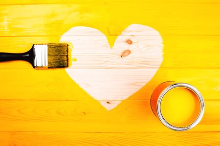 Heart shape of wooden background with brush and open can inside freshly painted yellow surface. Renovation concept.の写真素材