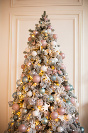 White coniferous tree decorated with glittering balls and shiny light garland on Christmas day