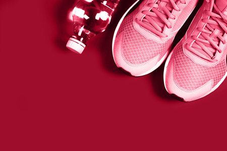 Sneakers and bottle of water on red background. Concept of healthy lifestile, everyday training and force of will. Demonstrating Viva Magenta - trendy color of the year 2023の写真素材