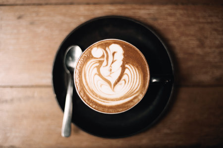 Artistic latte with foam design served in a black cup on tableの写真素材