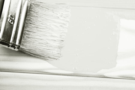Paintbrush applying white paint to wooden surface.の写真素材