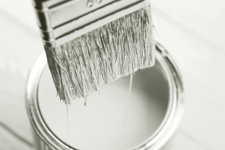 Paintbrush dripping paint into open can in monochrome.の写真素材