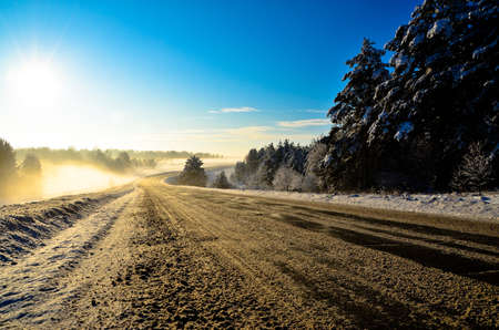 road in winter. sunrise and morning fog. trees grow on the roadside.