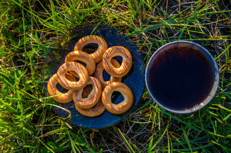 on a green lawn in the early foggy morning . all the grass in the morning dew . the sun's rays fall on the wet grass and flowers. tea in a cup with bagels .の写真素材
