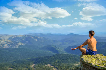 on top of a high mountain cliff in front of a man sitting in the lotus position and meditates. a man sitting on top of a mountain in the lotus position.の写真素材