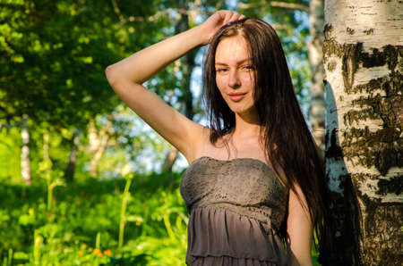 Brunette stands near the birch in forest. girl walking on the green forest. girl in short summer dress in nature .の写真素材
