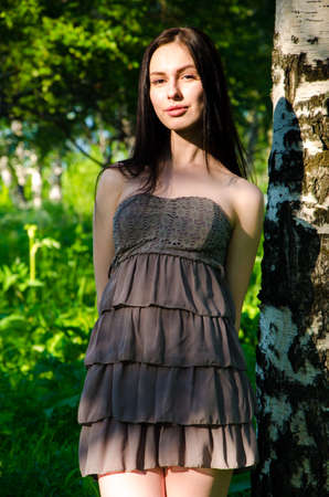 Brunette stands near the birch in forest. girl walking on the green forest. girl in short summer dress in nature .の写真素材