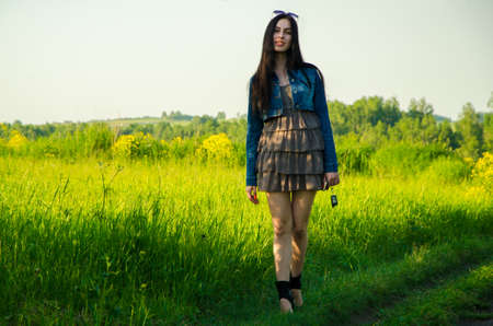 Brunette walks on a green meadow with sunglasses. beautiful brunette girl in a short summer dress walking on green grass path .の写真素材