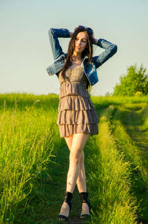 Brunette walks on a green meadow with sunglasses. beautiful brunette girl in a short summer dress walking on green grass path .の写真素材