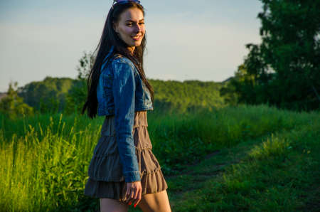 Brunette walks on a green meadow with sunglasses. beautiful brunette girl in a short summer dress walking on green grass path .の写真素材