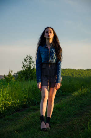 Brunette walks on a green meadow. girl in sunglasses. brunette in a short summer dress . girl in a summer dress walking on green grass . the path is a beautiful girl .の写真素材