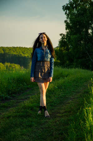 Brunette walks on a green meadow with sunglasses. beautiful brunette girl in a short summer dress walking on green grass path .の写真素材