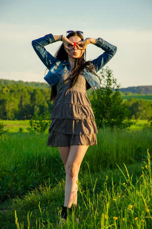 Brunette walks on a green meadow with sunglasses. beautiful brunette girl in a short summer dress walking on green grass path .の写真素材