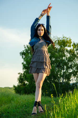 Brunette walks on a green meadow with sunglasses. beautiful brunette girl in a short summer dress walking on green grass path .の写真素材