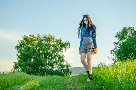 Brunette walks on a green meadow with sunglasses. beautiful brunette girl in a short summer dress walking on green grass path .の写真素材