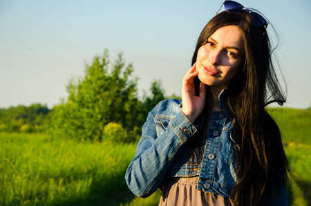 Brunette walks on a green meadow with sunglasses. beautiful brunette girl in a short summer dress walking on green grass path .の写真素材