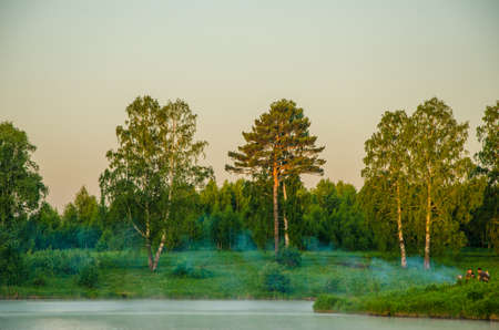 fog over the water . morning fog. thick morning mist over the lake . around the lake grow birch . landscape early in the morning warm . the sun rises and lights up the forest with a pond in the fog .の写真素材