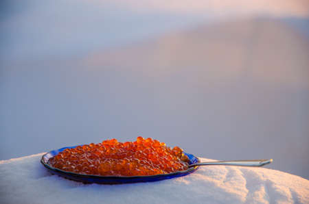 red caviar in the snow. blue plate with metal spoon
