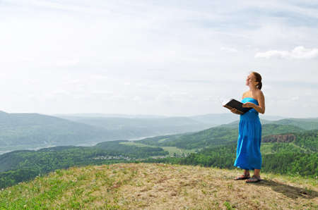 Red haired woman with book on the hilltop.の写真素材
