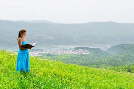 Red haired woman with book on the hilltop.の写真素材