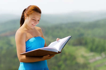 Red haired woman with book on the hilltop.の写真素材
