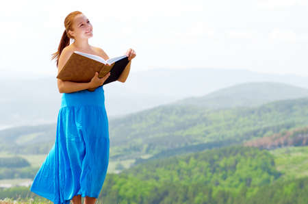 Red haired woman with book on the hilltop.の写真素材