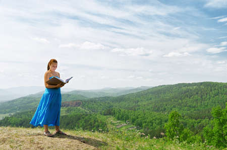 Red haired woman with book on the hilltop.の写真素材