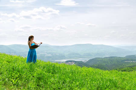 Red haired woman with book on the hilltop.の写真素材