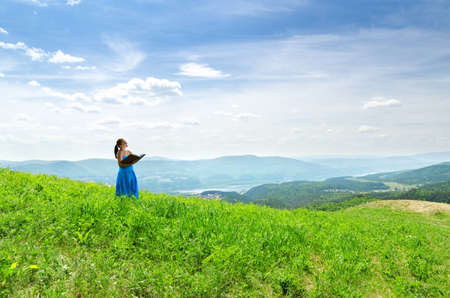 Red haired woman with book on the hilltop.の写真素材