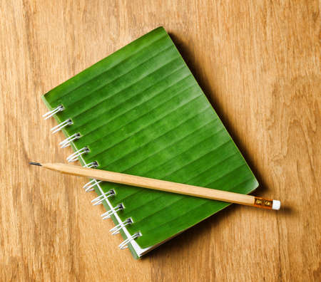 Notepad with cover of leaf lies on wooden board.の写真素材