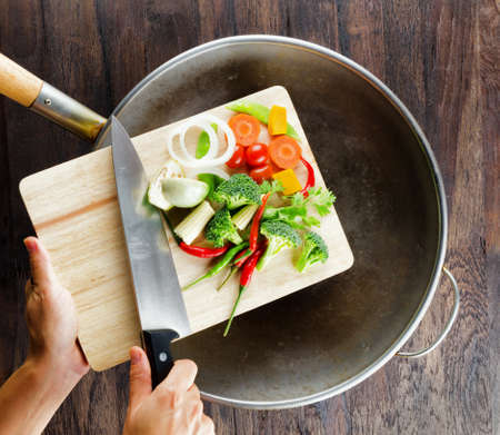 Fresh vegetables on the cutting board are falling in the wok. Concept of cooking.の写真素材