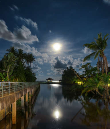 Gazebo and moon in water's reflection. Night landscape.の写真素材