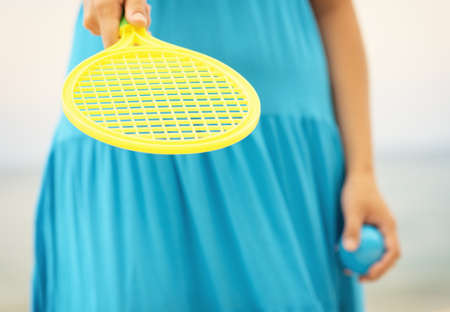 Woman in blue dress playing tennis on the beach.