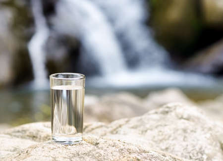 Glass of water by waterfall.の写真素材